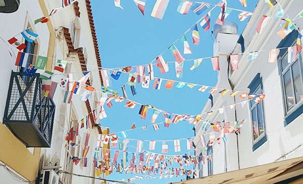 Various small international flags hang between buildings above a street. Public domain image.